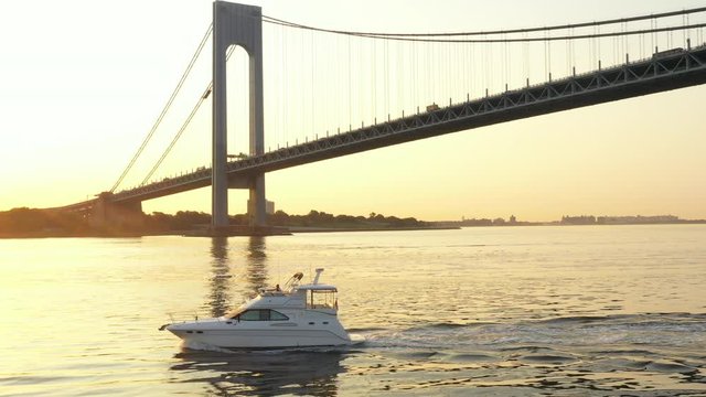 Low side tracking aerial of yacht with camera is tilted up to see silhouette-like Verrazano Bridge in background; nie and smooth