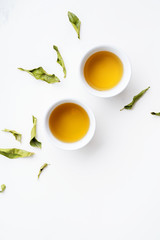 Asian tea concept, two white cups of tea and teapot surrounded with dry green tea  leaves , space for a text on white background. Brewing and Drinking tea.
