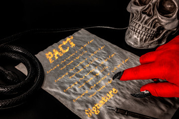 Pact or deal with the devil, faustian bargain and selling one's soul to Satan concept with red hand with claws pointing to a contract written in fire surrounded by a skull (death) and a snake (deceit)