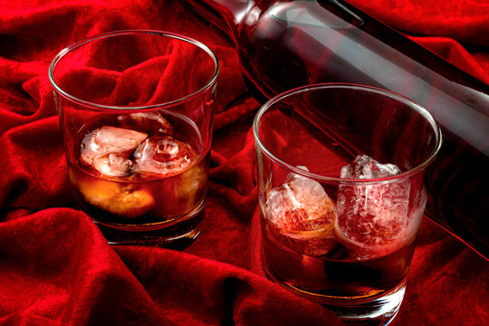 Alcoholism And Nightcap Drink Concept Theme With Close Up On An Expensive Bottle Of Single Malt Scotch And Two Glasses Of Whiskey On The Rocks On Red Velvet Background