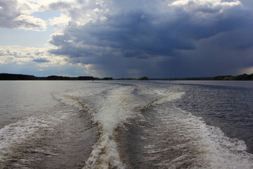Dark stormy sky with heavy clouds over the water on outboard motor yacht trail background, beautiful river landscape on a summer day