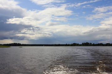 Stormy blue sky with dark clouds over the water, beautiful river landscape on a summer day