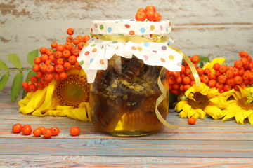 A jar of honey and bee honeycombs is on the table. Rowan fruits, horizontal composition. Foreground. Sunflower flowers.