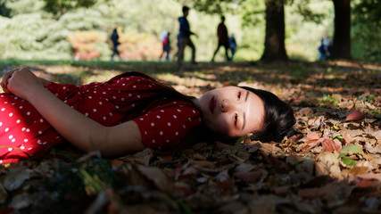 Portrait of beautiful young brunette woman in red dress lying on ground in forest park in sunny summer day. Outdoor fashion portrait of glamour Chinese stylish lady. Beauty, lifestyle Concept.