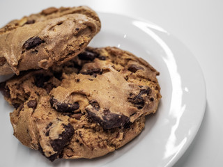 Closeup​ shot​ of​ two​ pieces of​ chocolate cookie on​ white​ plate and​ white​ table.