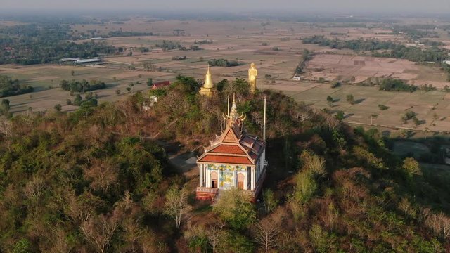 Aerial drone view orbiting Buddhist pagoda on forest mountain temple in rural Asia. Golden Buddhist statues can be seen in the background.