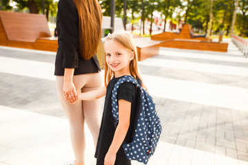 Mom leads her daughter to school. Return to school. Woman and girl with backpack behind the back. Beginning of lessons. First day of fall.