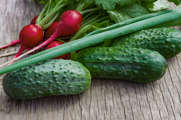 Fresh small green cucumbers with radishes and green onions on an old wooden table, summer vegetable harvest close-up