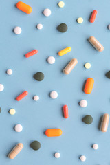 Different size and color pills on blue background.
