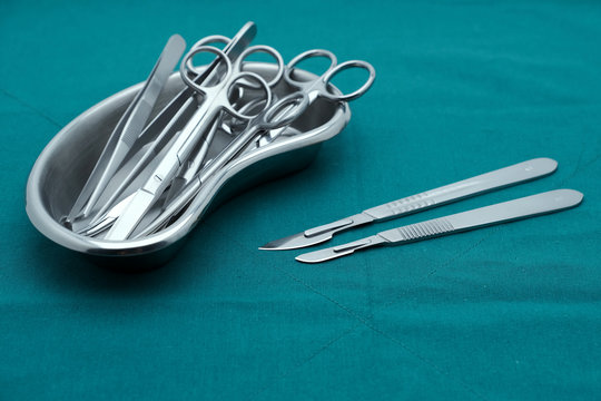 Basic surgical instrument forceps tweezers scissors in emesis or plus basin and scalpel on surgical green drape fabric