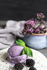 Berry ice cream. Decorated with blackberries and mint leaves. Ceramic plate. Gray concrete background.