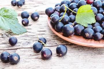 Fresh ripe currant berries in a bowl on wooden background near green leaves. Juicy fruits currants. Black currant