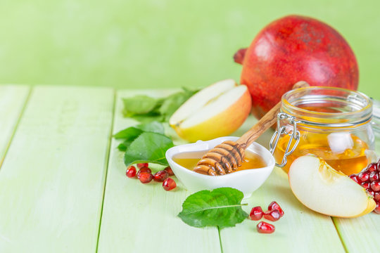 Rosh hashana jewish holiday concept - apples, honey, pomegranate, green wood background