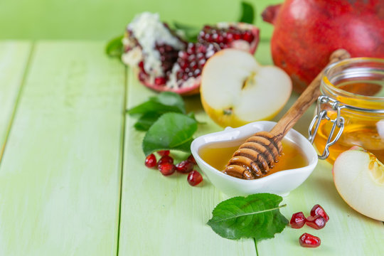 Rosh hashana jewish holiday concept - apples, honey, pomegranate, green wood background