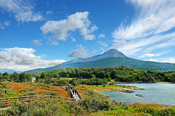 Panoramic view of Tierra del Fuego National Park, showing a volcano surrounded by green vegetation and water, against a blue sky. - obrazy, fototapety, plakaty