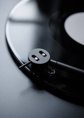 Modern round headshell with cartridge on straight tonearm and vinyl record disc with white label...
