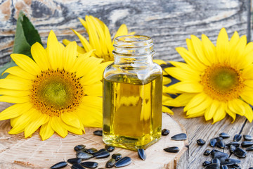 Organic sunflower oil in a glass jar with seeds and fresh flowers on a wooden background. Healthy...