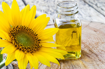 Sunflowers on a wooden background near sunflower oil in a glass jar. Healthy foods and fats.