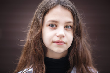 close-up portrait of little beautiful stylish kid girl with long flowing hair against a brown striped wall