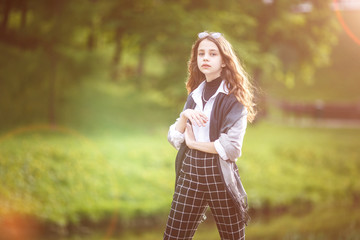 portrait of little beautiful stylish kid girl with sunglasses and short plaid pants in city park on...