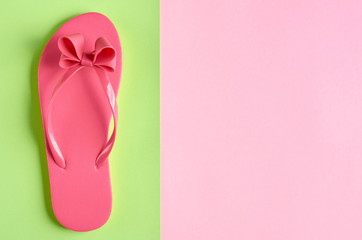 Pink rubber slippers on green background composition.