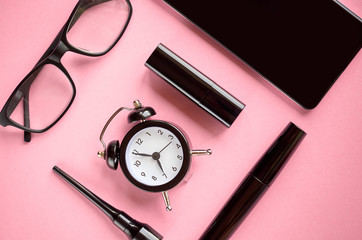 Black glasses, alarm clock, cellphone, mascara and pomade on pink background composition.