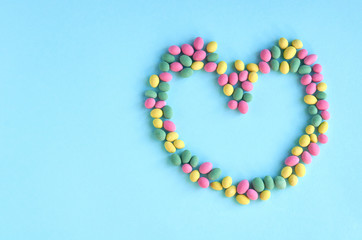 Colored sweets, peanut covered with glaze on blue background composition, heart shape, frame.
