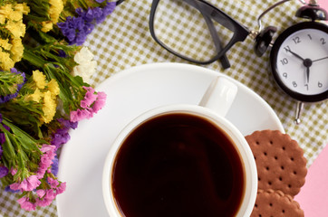 Coffee cup with cookies, alarm clock, flowers, mascara, on pink background composition.