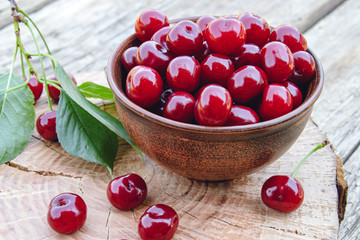 Red cherry in a bowl and green leaves on old wooden boards. Juicy delicious fruit.