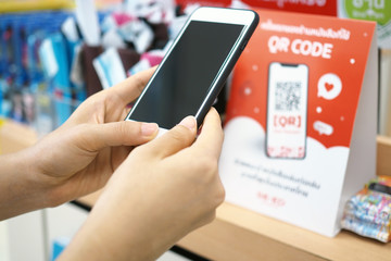 Hands use the phone to scan the QR code to receive discounts on purchases in the department store.