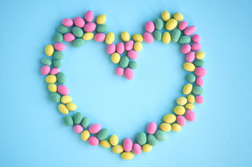 Colored sweets, peanut covered with glaze on blue background composition, heart shape, frame.