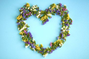 Colored flowers on blue background composition, heart shape. Flat lay