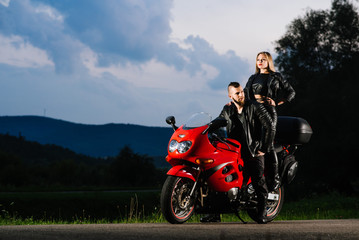 Fototapeta na wymiar Cool biker couple in leather jackets sitting on red sports bike outdoors