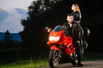 Obraz na płótnie Canvas Cool biker couple in leather jackets sitting on red sports bike outdoors