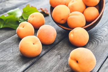 Delicious ripe apricots in a bowl next to green leaves on a wooden table.