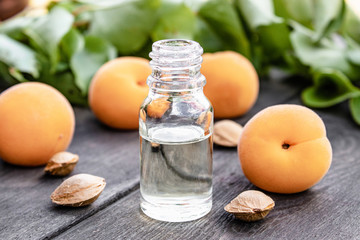 Apricot oil in a glass jar close-up on a table near a ripe yellow apricot.
