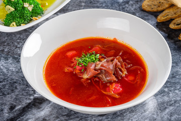 Close up view on Traditional Ukrainian borsch with smoked duck. Modern ukrainian cuisine. Red soup in white plate on marble plate. Food for lunch. Copy space