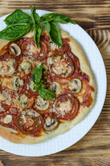 Pizza with mushrooms and tomatoes, basil on a white plate on a wooden background top view