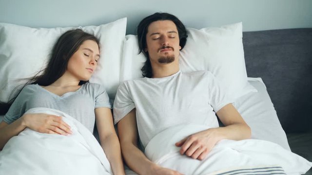 Young attractive man and woman sleeping in bed at home resting together in cozy bedroom wearing pajamas. Relaxation, apartment and lifestyle concept.