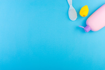 Flat lay composition of baby care products on a blue background. View from above shampoo or shower bottle gel, cleaning brush and yellow rubber toy duck
