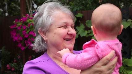 Happy and Beautiful Grandmother with short Silver Hair playing in the Garden with her 4 Month Old Cute Granddaughter. Happy Family Concept