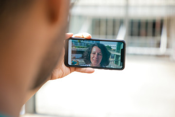 Speaking woman on mobile phone screen communicating through video call. Man holding smartphone and talking to his wife. Distance relations concept