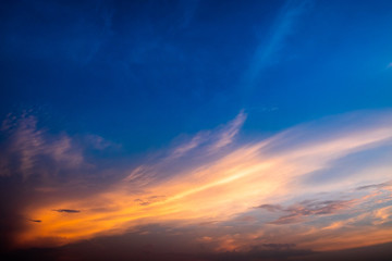 Twilight clear blue sky with dramatic orange sunlight in diagonal pattern and white clouds.