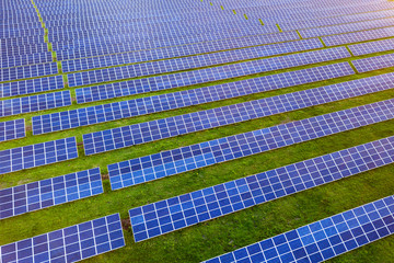 Large field of solar photo voltaic panels system producing renewable clean energy on green grass background.
