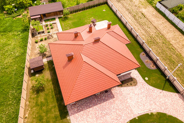 Aerial top view of new residential house cottage with shingle roof on fenced big yard on sunny day.