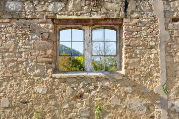 Vieille fenêtre sur un mur en vieilles pierres donnant sur un jardin
