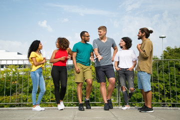 Multiethnic team of friends chatting on bridge. Mix raced group of young people standing on bridge outdoors, talking, listening, gesturing. Team of friends concept