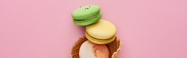 top view of multicolored delicious French macaroons in crispy waffle cone on pink background, panoramic shot