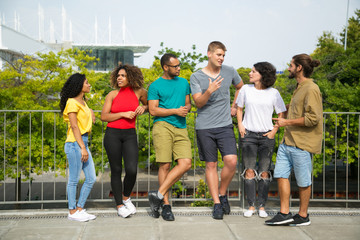 Obraz premium Interracial team of friends chatting together outside. Mix raced group of young people standing outdoors, talking, listening, gesturing. Team of friends concept