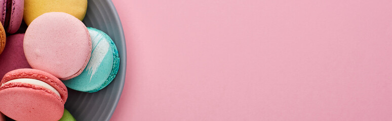 close up view of multicolored delicious French macaroons on plate on pink background, panoramic shot
